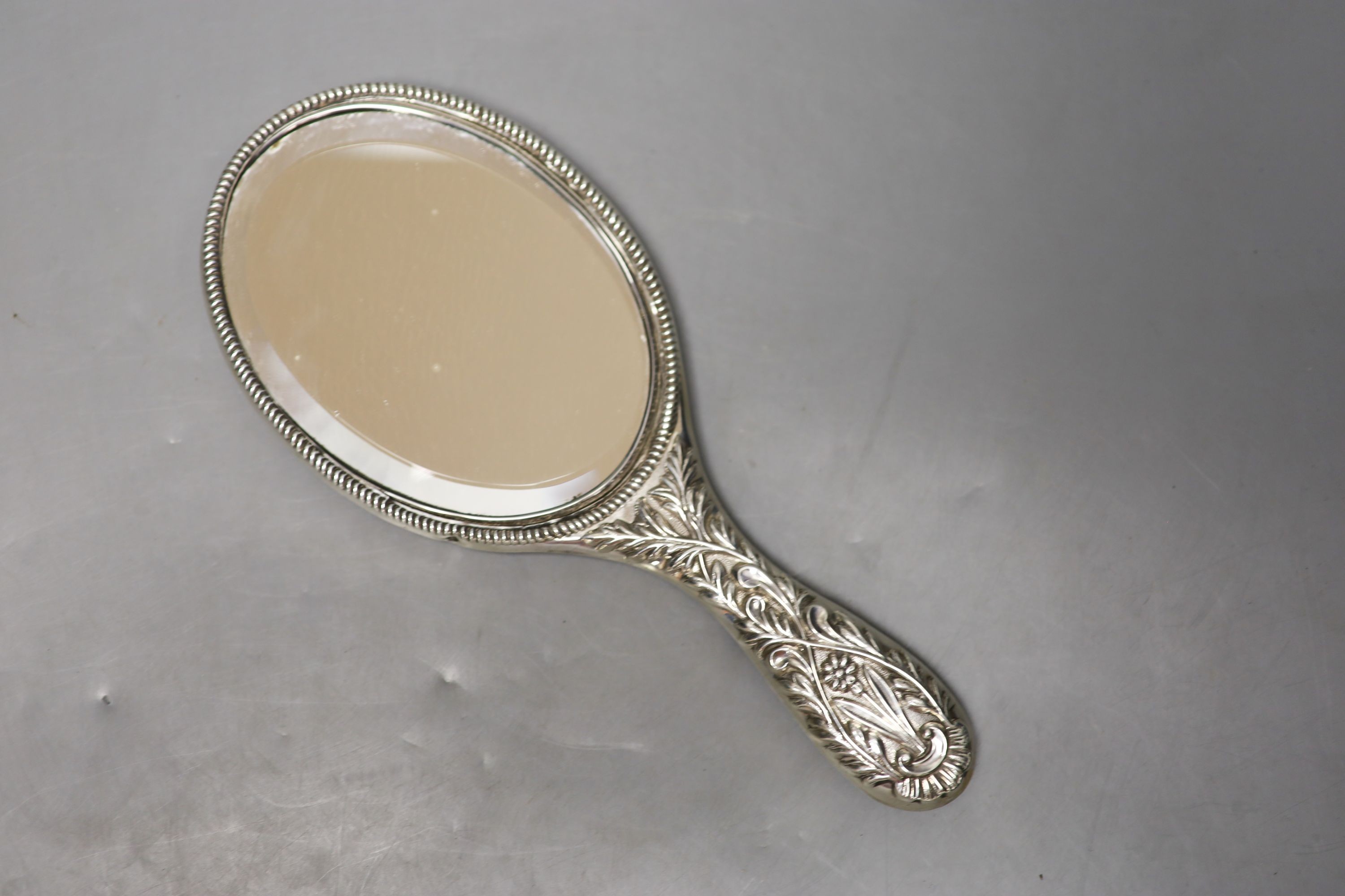 A late Victorian repousse silver mounted hand mirror, London, 1899, two silver mounted glass toilet jars, a silver handled button hook, silver handled shoe horn and a clothes brush.